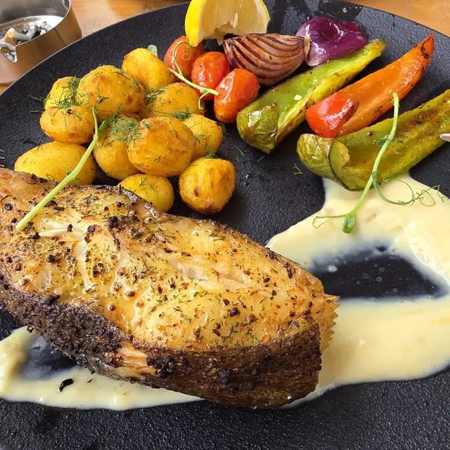 Halibut z grillowanymi warzywami i ziemniakami na czarnym talerzu